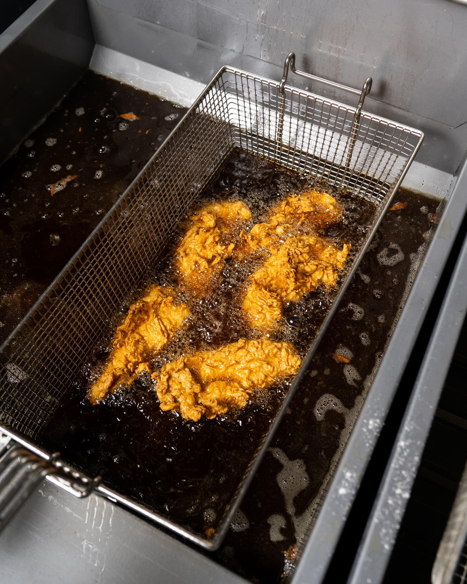 Chicken pieces submerged in a beef tallow fryer