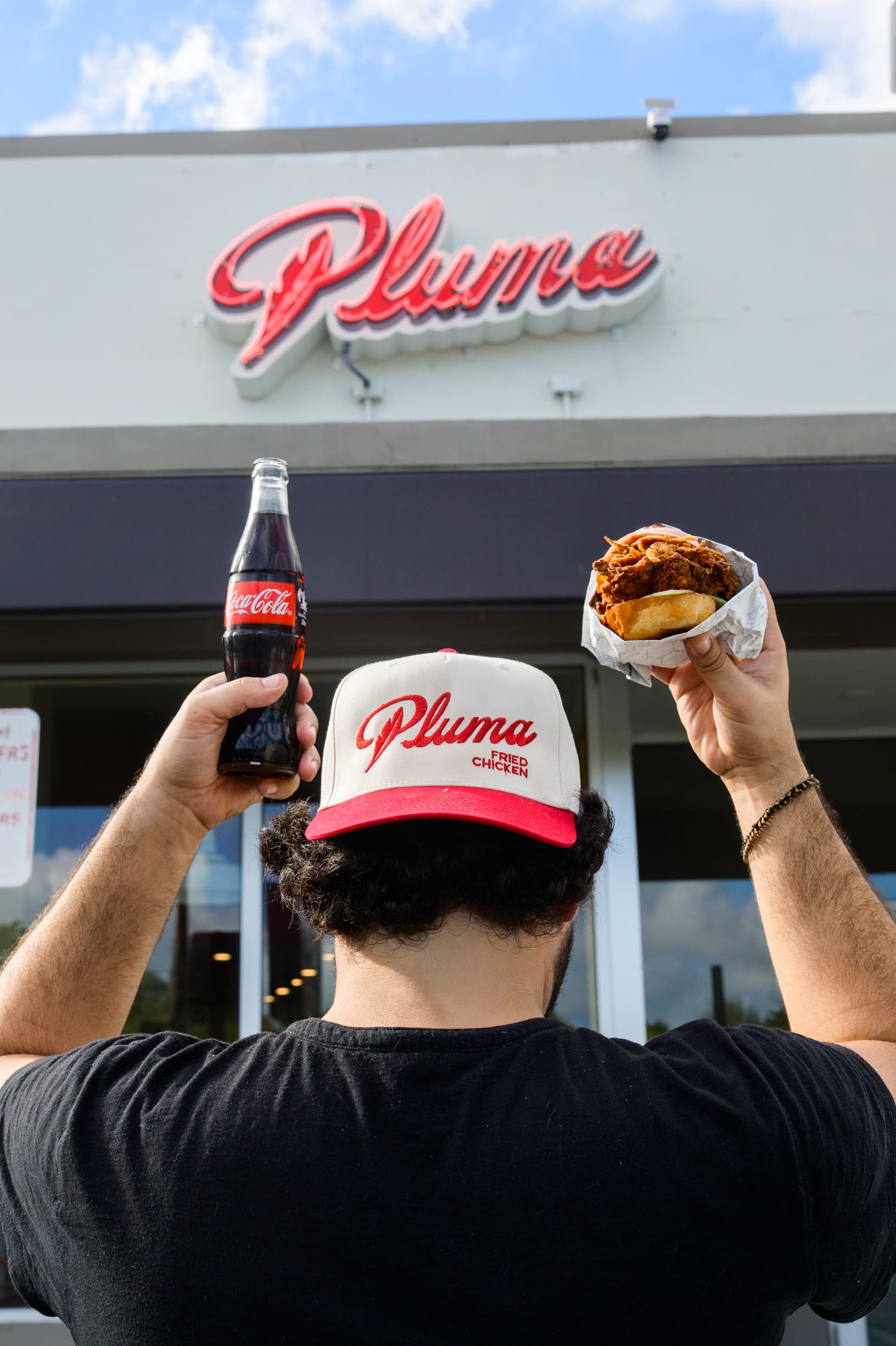Guest holding a Pluma fried chicken sandwich and a Coke outdoors